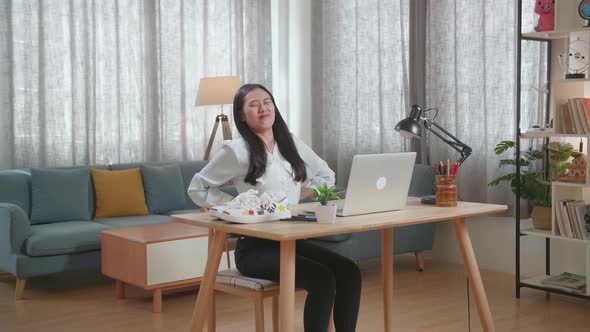 Asian Female Footwear Designer Having A Backache While Working On A Laptop At Home