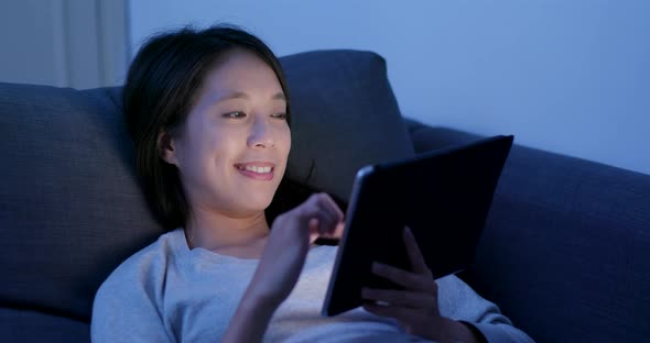 Woman use of tablet computer and lying on sofa at night