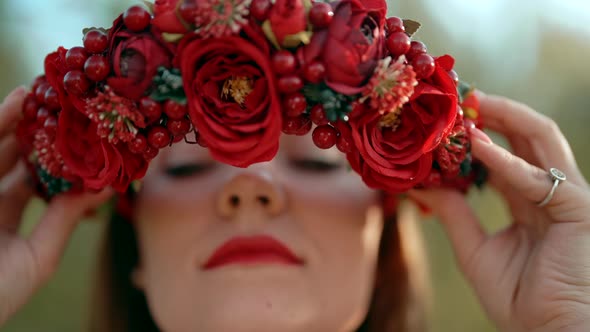Ukrainian Woman Puts on Head Wreath From Red Flowers and Viburnum