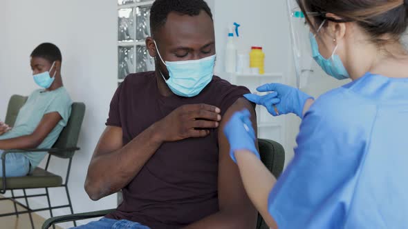 Female doctor vaccinating young black male patient