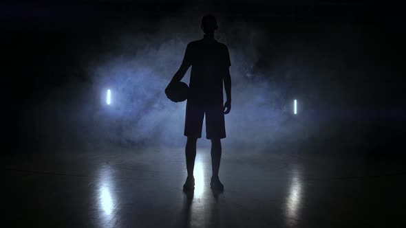 The Silhouette of a Basketball Player on a Dark Background with Smoke on the Basketball Court Throws