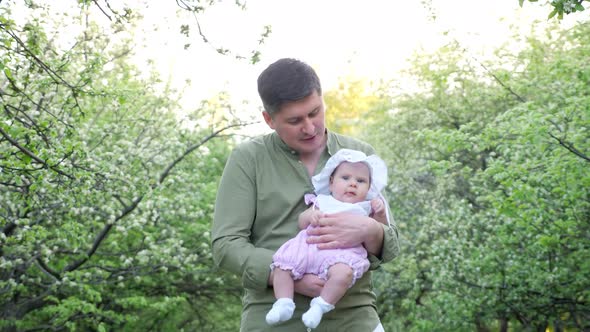 Smiling Father in Green Shirt Holds Baby Daughter in Arms