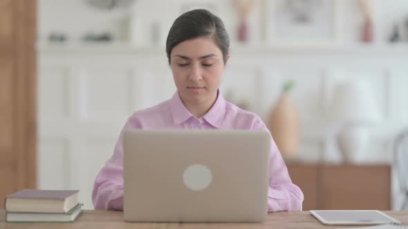 Indian Woman Looking at Camera while using Laptop in Office