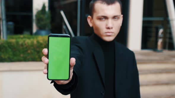 Young Caucasian Man Showing Mobile Phone with Green Screen at Urban City Business Center