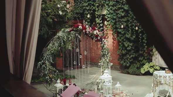 Wedding Arch with Red Flowers and White Chairs Lamp Garland Over the Ceremony Near Restaurant Slow