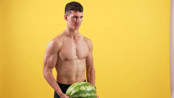 Muscular Man Lifting Heavy Water Melon for Biceps Muscles on Yellow Background Sport
