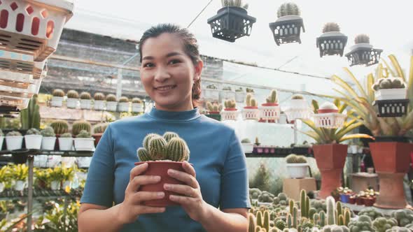 Portrait of beautiful young Asian girl showing indoor cactus plant in flowerpot. Closeup.