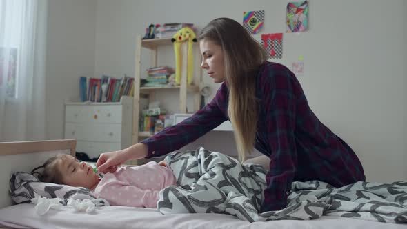 Mom Measures the Temperature of a Little Girl Lying Sick in Bed