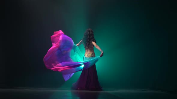 Woman with a Veil in Her Hands Dancing Belly Dance. Smoke Background