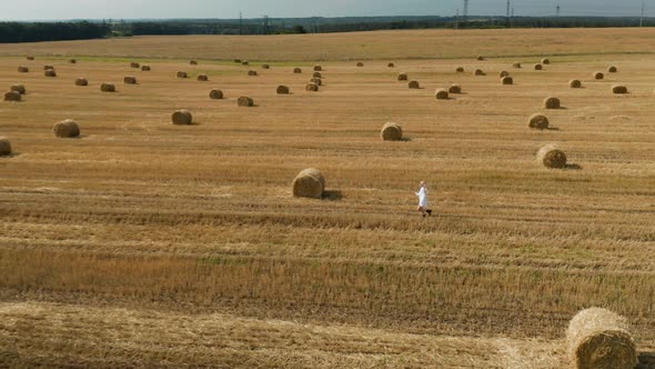 Beautiful young girl in a white shirt on a field among sheaves of hay. Aerial view	