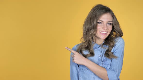 Young Girl Pointing with Finger on Side, Yellow Background