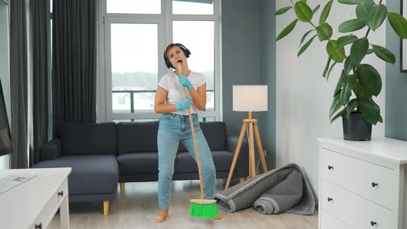 Woman in Headphones Cleans the House and Have Fun Singing with a Broom Like a Star at a Concert