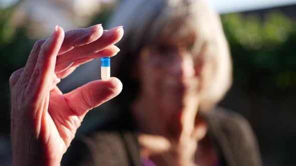 An old woman holding a prescription medication drug pill to improve her health and cure illness.