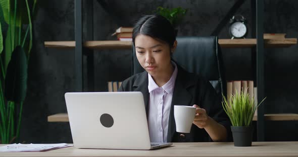 Young Asian Attractive Female Office Worker Sitting at the Laptop Computer at the Desk Working and