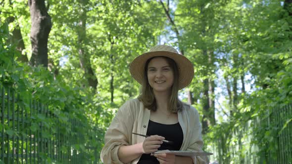 Professional Lady Artist in Brown Straw Hat Paints Artwork