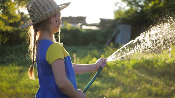 Funny Little Girl in Hat Playing with Garden Hose in Sunny Backyard. Adorable Little Girl Playing