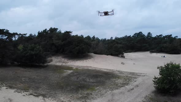 Looking at drone flying up above fields of grass and heather and banks of sand. Drone is a little sh