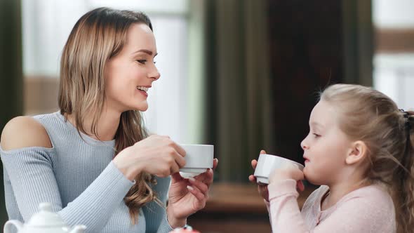 Beautiful Young Mom Talking with Cute Daughter Drink Tea