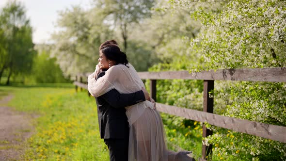 Joyful and Playful Lady is Embracing and Kissing Her Husband During Walk in Nature