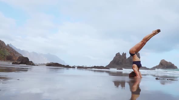 Beautiful Woman on the Ocean Beach with Black Sand Performs Gymnastic Exercises Practicing a Healthy