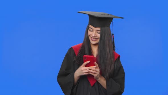 Portrait of Female Student in Cap and Gown Graduation Costume Texting on Her Phone