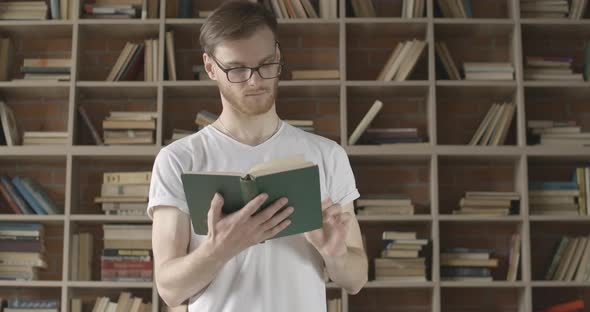 Middle Shot of Confident Caucasian Man in Eyeglasses Turning Book Page and Smiling