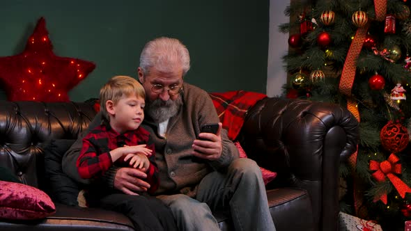 Elegant Old Man and Little Boy Browsing Content on a Smartphone and Having Fun