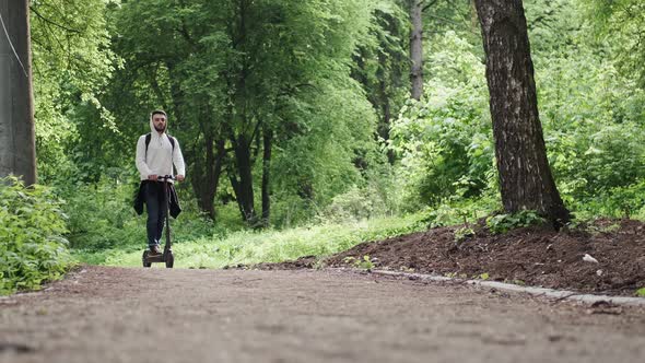 The Guy Rides an Electric Scooter in the Summer Forest