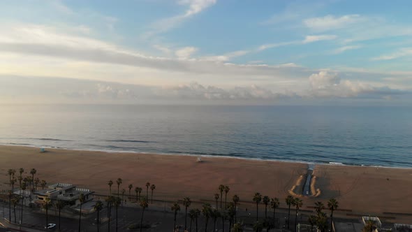 4k ariel drone pan of the stunning horizon, beach, pier, and surfers surfing as families vacation in