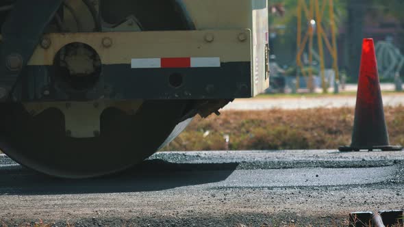 Close Shot of a Steam Roller Flattening a Newly Laid Road Surface by a Traffic Cone