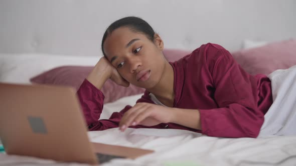 Bored Young African American Woman Putting Head on Bed Closing Eyes Working Online From Home Office