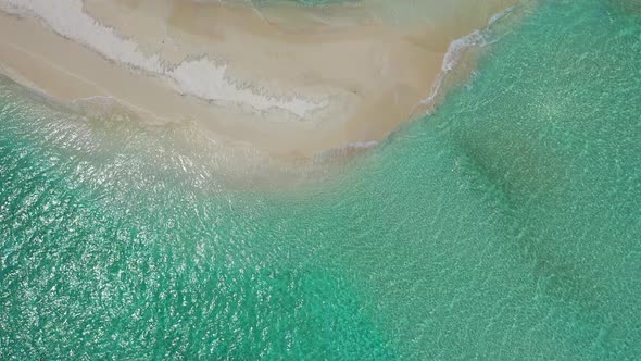 Wide flying tourism shot of a white sandy paradise beach and aqua blue water background in 4K