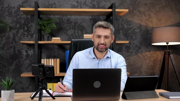 Smiling Man Stock Trader Listens Investor Online Laptop Makes Notes in Notebook