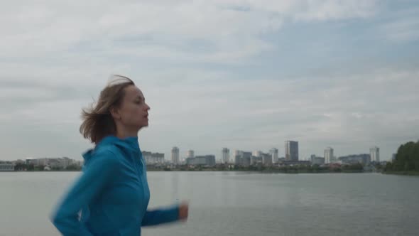 Young Sportswoman in Sportswear Trains in a Park Near the River