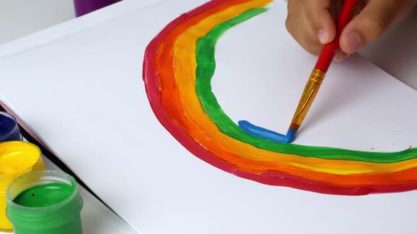 The girl draws a rainbow on paper with multicolored paints. Drawing with the eyes of a child