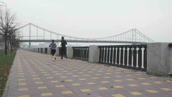 Running Sporty Couple Is Jogging on City Promenade Along River. Training for Marathon Concept