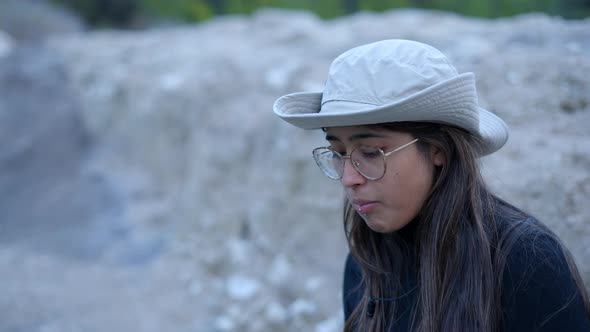 Close Side View of Young Woman in Hat and Glasses Eating in Nature