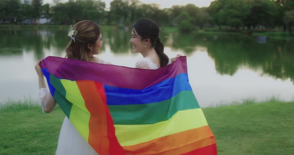 Asian Lesbian Couple With LGBT Flag Walking Together In The Park.