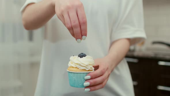 A Woman Holding a Cupcake in Her Hands and Decorating It in the Kitchen at Home