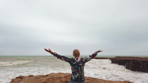 Girl Raises Her Hands Up While Standing with Her Back on the Seashore During a Storm.