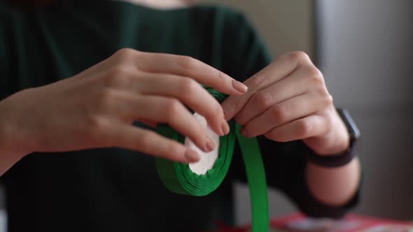 Closeup Hands of Unrecognizable Young Woman Twisting Satin Green Ribbon Into Roll Blurred Background