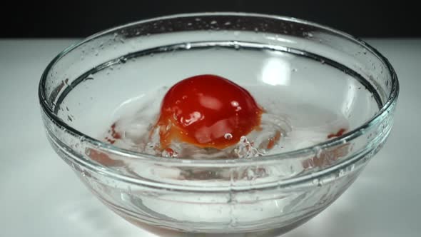 Ripe Juicy Tomato Falls Into a Clear Bowl of Clear Water on a White Background, Slow Motion