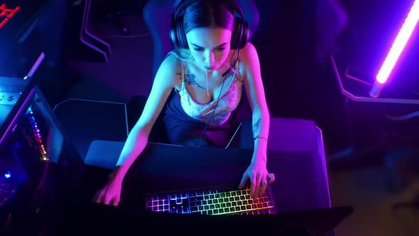 Gaming Concept - Young Attractive Gamer Woman Sits in the Chair in Neon Gaming Club and Playing