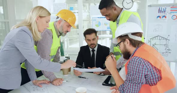 Team of Builders which Discussing Technical Drafts and Reports with their Confident Successful Boss