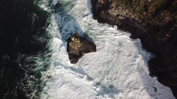 Rock next to the cliffs of Moher in the atlantic ocean, big waves create foam, drone aerial top view