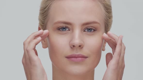 Studio portrait of young, beautiful and natural blond woman applying skin care cream. F