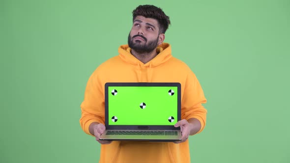 Happy Young Overweight Bearded Indian Man Thinking While Showing Laptop