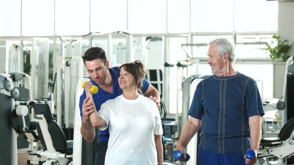 Personal Trainer Helping Lift Dumbbells To Seniors.