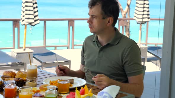 Young Man Eating Brunch at Restaurant in Tropical Hotel with Turquoise Sea Background