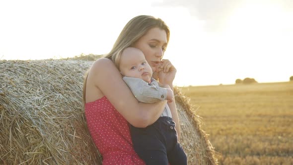 Happy Mother Having Joy with Her Little Son at Haycock in Field on Sunset